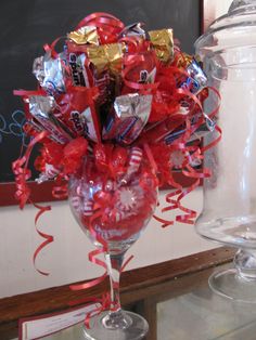 a glass vase filled with candy and wrapped in red ribbon, next to a chalkboard