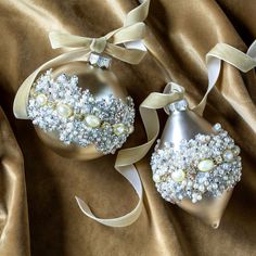 two christmas ornaments with pearls and bows on a satin background