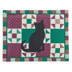 a black cat sitting on top of a green and purple patchwork placemats