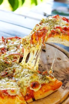 a slice of pizza is being lifted from a tray on a wooden table with greenery