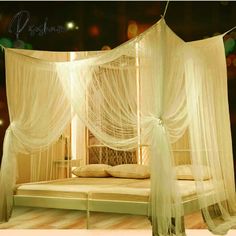 a canopy bed with sheer curtains and pillows on top of it in a room that is lit up at night