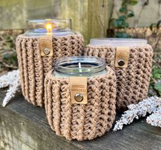 three crocheted mason jars sitting next to each other on a wooden table with a candle in the middle