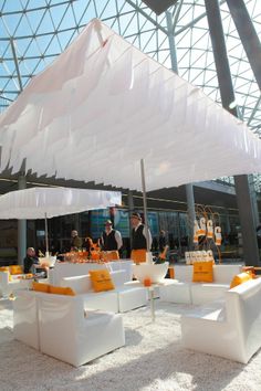 an outdoor event with white couches and orange pillows on the floor under umbrellas