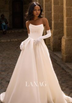 a woman in a white wedding dress standing on a cobblestone street wearing gloves