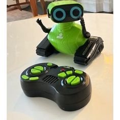 a green robot sitting on top of a table next to a controller