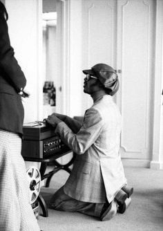 a man sitting on the floor playing an old fashioned record player with another person standing behind him