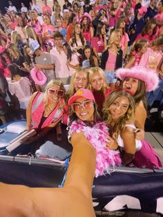 a group of women in pink hats and sunglasses taking a selfie at a sporting event