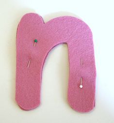 a pink felt letter with pins sticking out of it