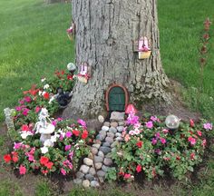 a fairy garden with flowers and rocks under a tree