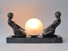 two statues sitting next to each other with a light on top of one that has a ball in front of it