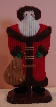 a knitted santa clause is sitting on top of a wooden stand with a bag