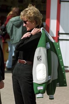 a woman holding onto a green and white jacket while standing next to another person in front of a building