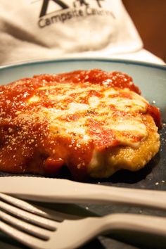 a piece of meat covered in sauce on a plate with a fork and knife next to it