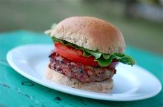 a hamburger with lettuce and tomatoes on a bun sitting on a white plate