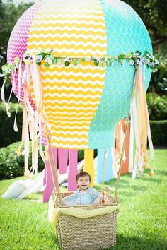 a baby sitting in a basket next to a hot air balloon