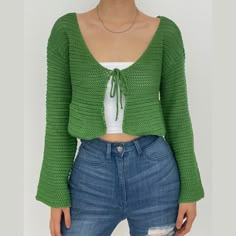 a woman wearing ripped jeans and a green cropped cardigan sweater is posing for the camera