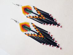 two pairs of beaded earrings with black, yellow and red beads on them sitting on a white surface