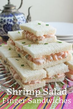 shrimp salad finger sandwiches stacked on top of each other in front of a teapot