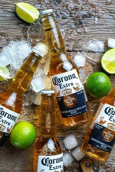 four bottles of corona extra beer surrounded by limes and ice