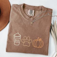 ❤️  EMBROIDERED Pumpkin Paw Coffee T-shirt, Dog Mom Gift, Dog Lover Gift, Cute Pumpkin Shirt, Fall Shirt, Pumpkin Spice and Dogs, Gift for Her ❤️ The cutest, embroidered T-shirt for dog lovers will have you ready for all of your upcoming fall activities! Featuring a delicate embroidery of pumpkin spice latte (yum a paw and a cute pumpkin, the t-shirt was handmade with love and durable materials to make sure it lasts.  KEY FEATURES:  Unisex (fits both men and women) Brand: Comfort Colors  Runs tr Fall Shirt Ideas, Dog Shirt Design, Embroidered Pumpkin, Cozy Fall Outfits, Etsy Ideas, Cute Shirt Designs, Dog Leashes, Delicate Embroidery, Coffee Shirt