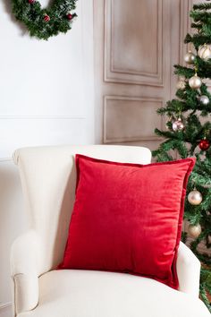 a red pillow sitting on top of a white chair next to a christmas tree and wreath