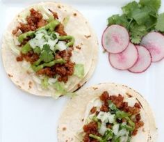 three tortillas on a plate with radishes and cucumbers next to them