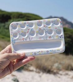 a hand holding an egg tray with six eggs in it and flowers on the outside