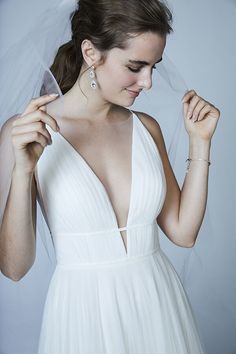 a woman in a white wedding dress is holding her veil over her head and looking down