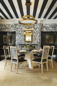 a dining room with black and white wallpaper, gold chandelier and chairs