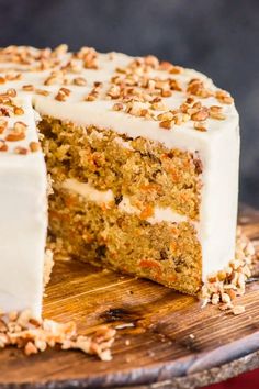 a carrot cake with white frosting and chopped nuts on a wooden cutting board next to a slice cut out