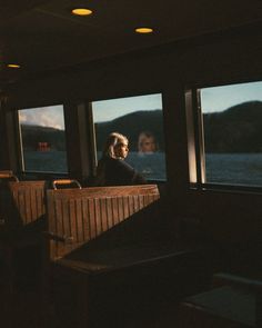 a woman sitting in a booth looking out the window at water and mountains behind her