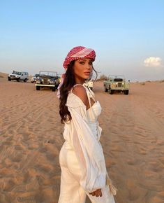 a woman standing on top of a sandy beach next to a green truck and jeep