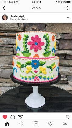 a three tiered cake decorated with flowers and leaves on a black stand in front of a stone wall