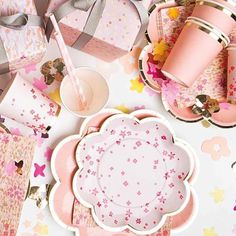 a table topped with pink plates and cups filled with paper flowers next to gift boxes