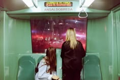 two women sitting on a bus looking at the street sign in an area with green walls