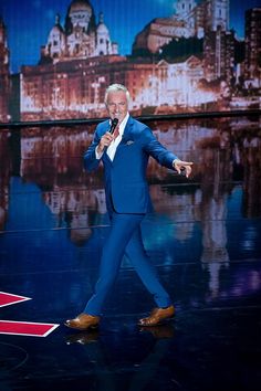 an older man in a blue suit and tan shoes is on stage with a microphone