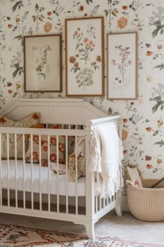 a white crib in front of floral wallpaper and framed pictures on the wall