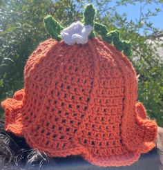 an orange crocheted hat with a flower on top, sitting in front of some trees