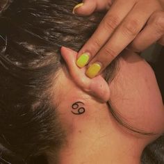 a woman with a small tattoo on her neck and behind her ear is a yellow manicure