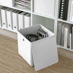 a white storage box sitting on the floor in front of a bookcase filled with books