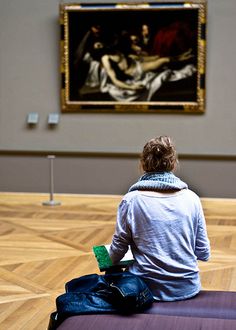 a woman sitting on top of a piece of luggage in front of a large painting