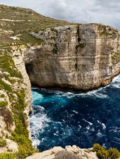 an ocean cliff with blue water and cliffs in the background