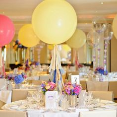 a table set up for a party with balloons in the air and flowers on it