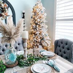 a dining room table decorated for christmas with silver and white decorations on it, including a small tree