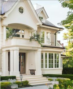 a large white house with lots of windows and plants on the front porch, along with steps leading up to it