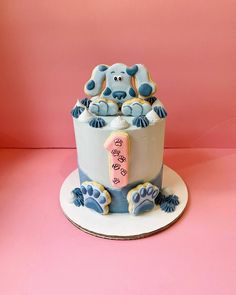 a blue and white cake with a dog on top sitting on a pink tablecloth