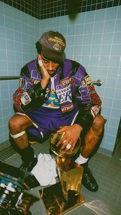 a man sitting on top of a toilet in a bathroom next to a trash can