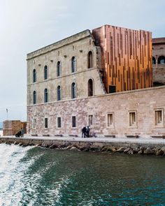 two people standing on the side of a body of water next to a large building