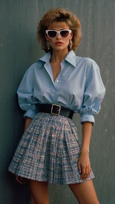 Woman wearing a classic 80s outfit with an oversized blue shirt, high-waisted pleated skirt, and statement earrings. 80s Glamour Fashion, 80s Upper Class Fashion, 80s Mini Skirt Outfit, 80s Pastel Fashion, Plaid 80s Outfit, 80s High School Fashion