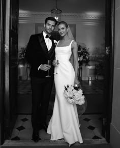 a man and woman in formal wear posing for the camera while holding champagne glasses together